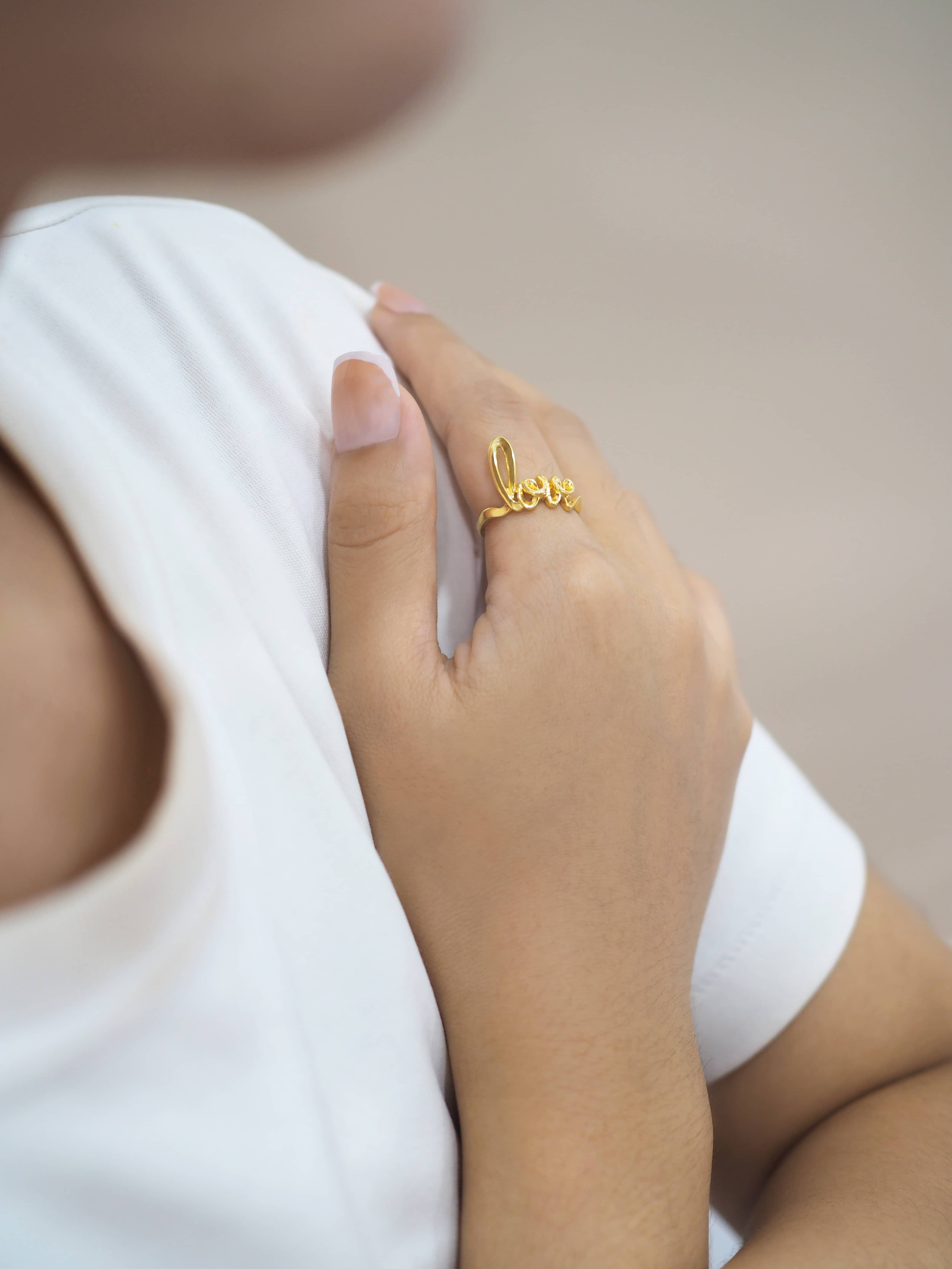 Close-up of a hand wearing a gold ring with the word 'love'