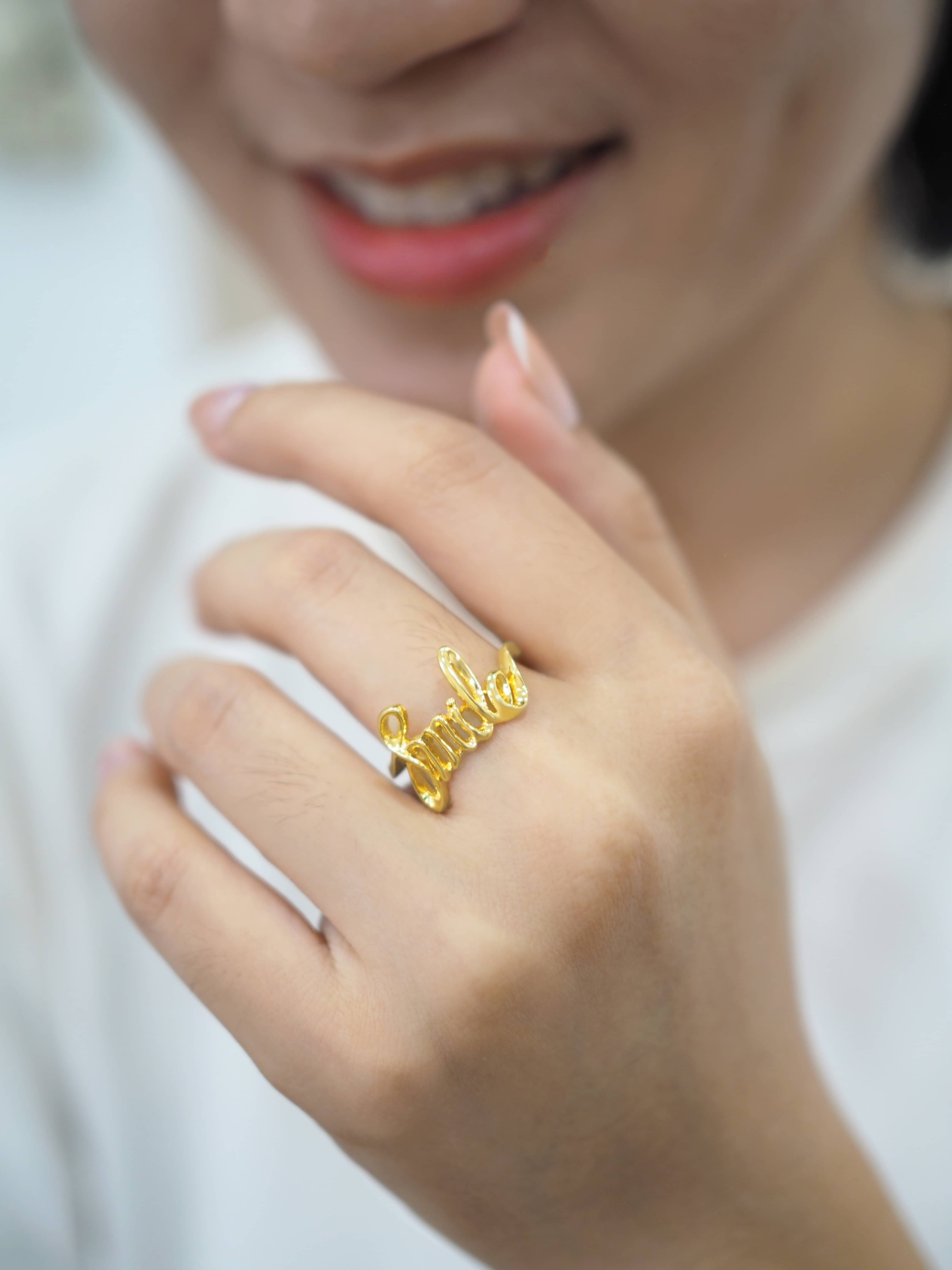 Close-up of a hand wearing a gold ring with the word 'smile'