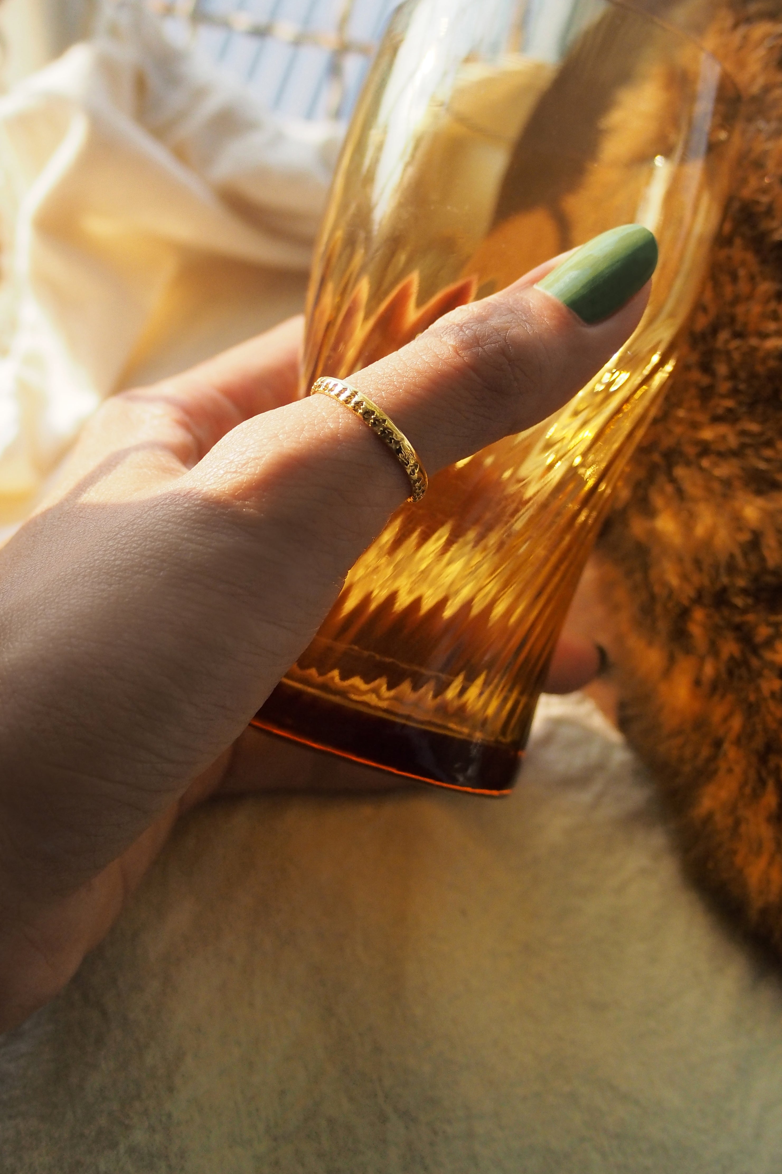 Close-up of a hand adorned with a minimal gold ring holding a glass.