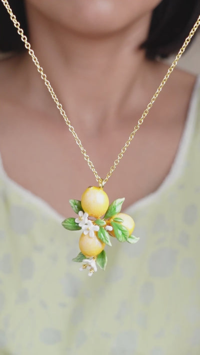 A close-up of a person wearing a gold chain necklace with lemon charms and white flower accents, ideal for summer fashion.