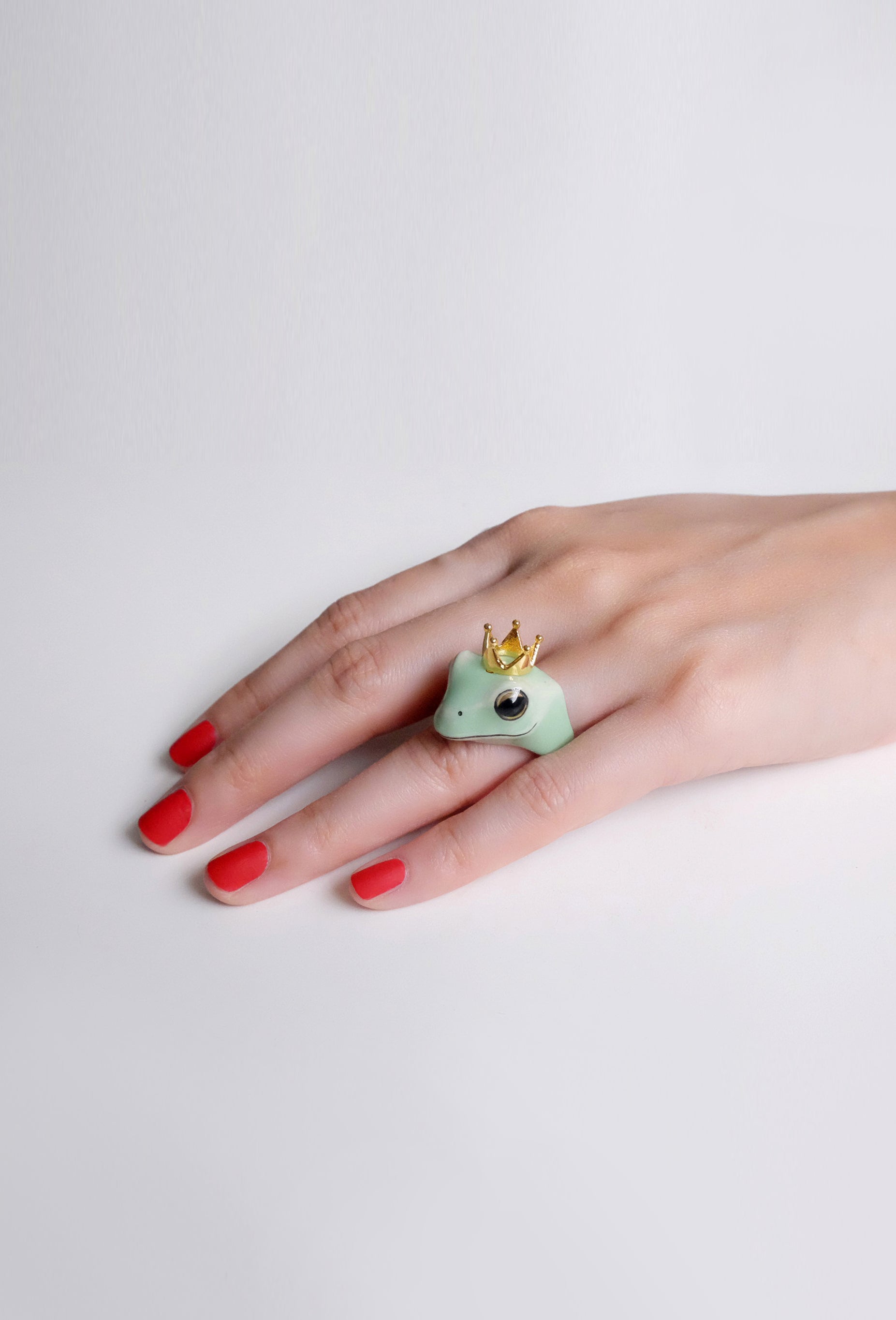 A playful frog ring with a crown on a hand with red nails.