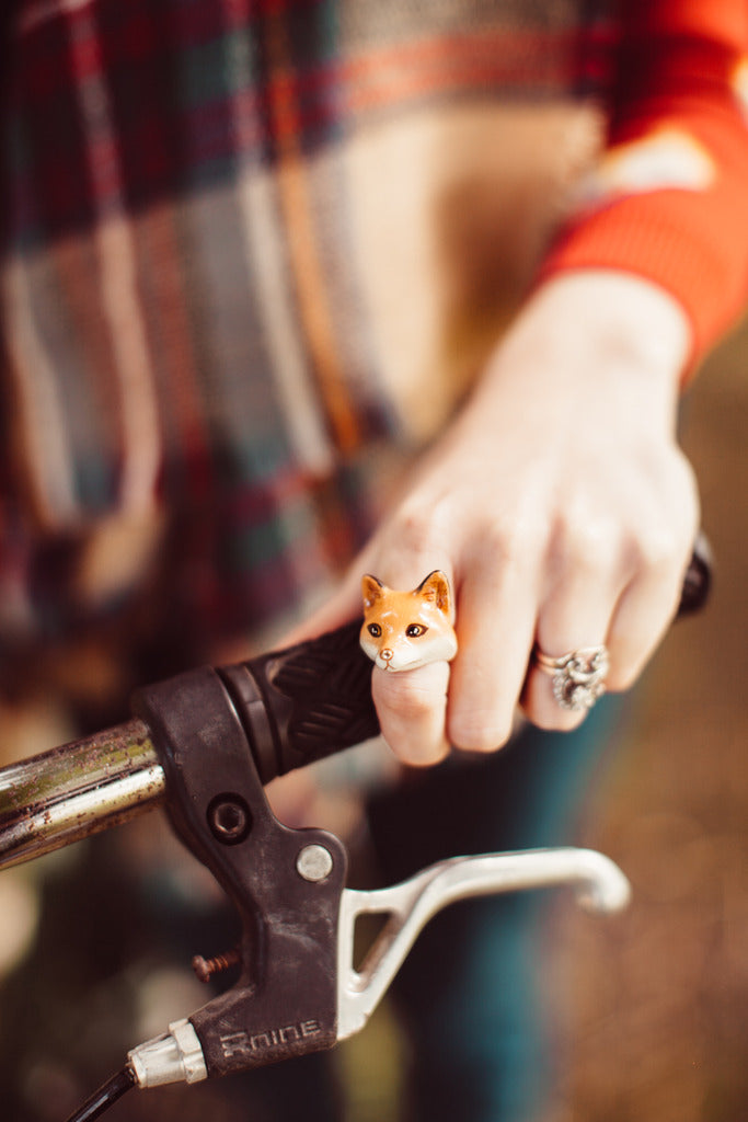 A hand holding a bike handlebar adorned with a red fox-shaped ring.
