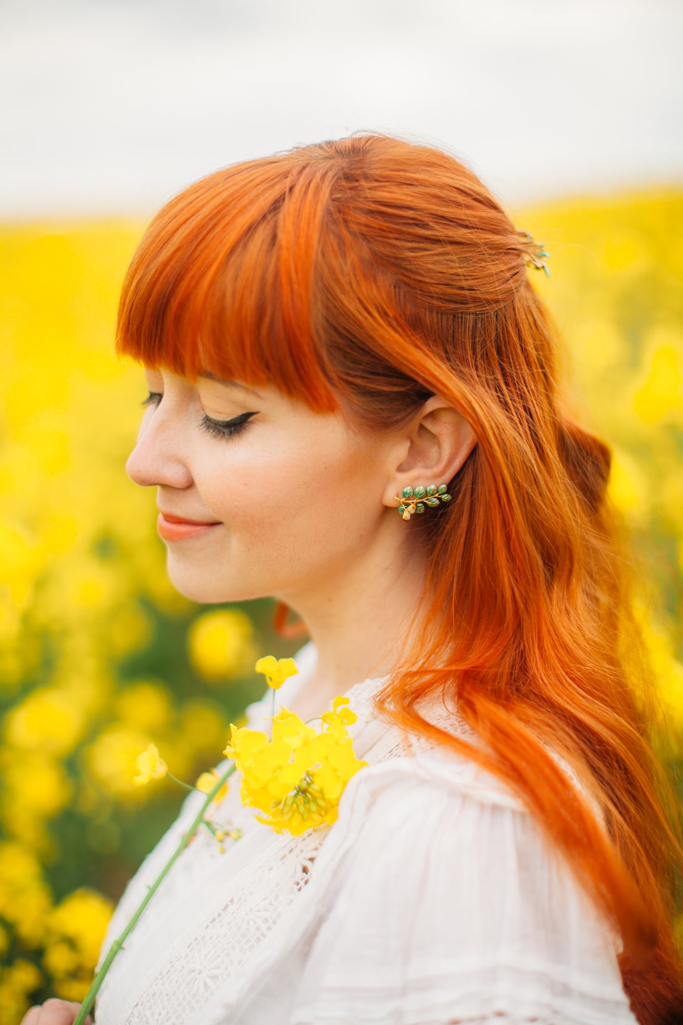 A red hair woman wearing nature-inspired earrings in a blooming field.