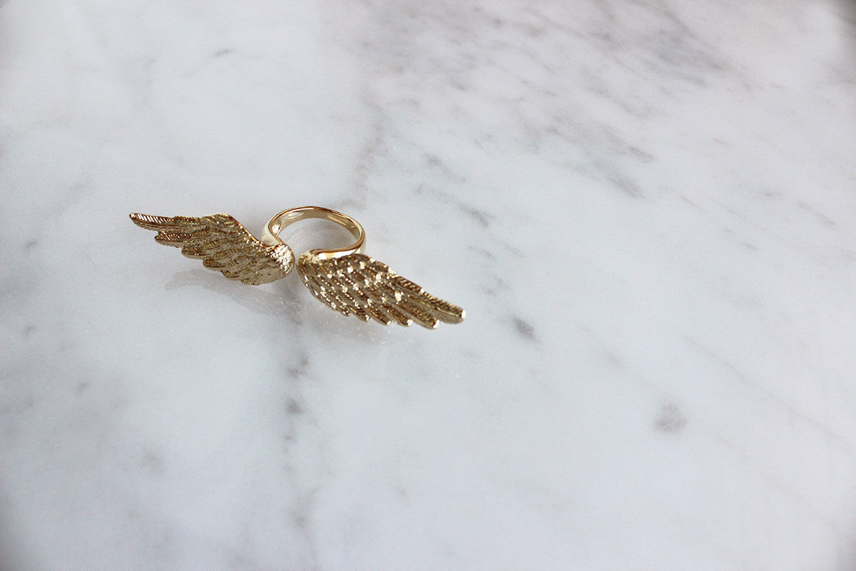 Artistic angel wing ring displayed on a marble background.