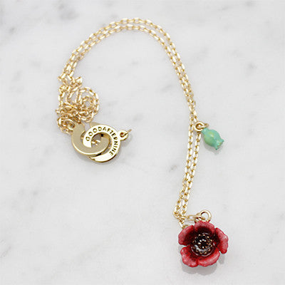 Gold necklace featuring a red flower pendant and a small green accent, placed on marble background