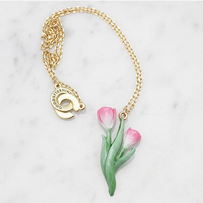A floral necklace featuring pink tulip and green leaves on a gold chain, placed on a marble background.