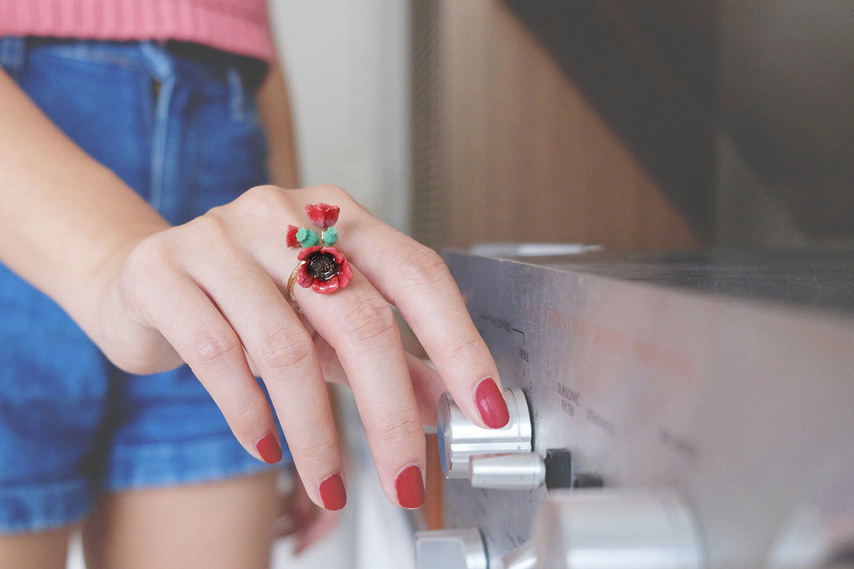 Close-up of a hand with red nail polish wearing a red poppy ring