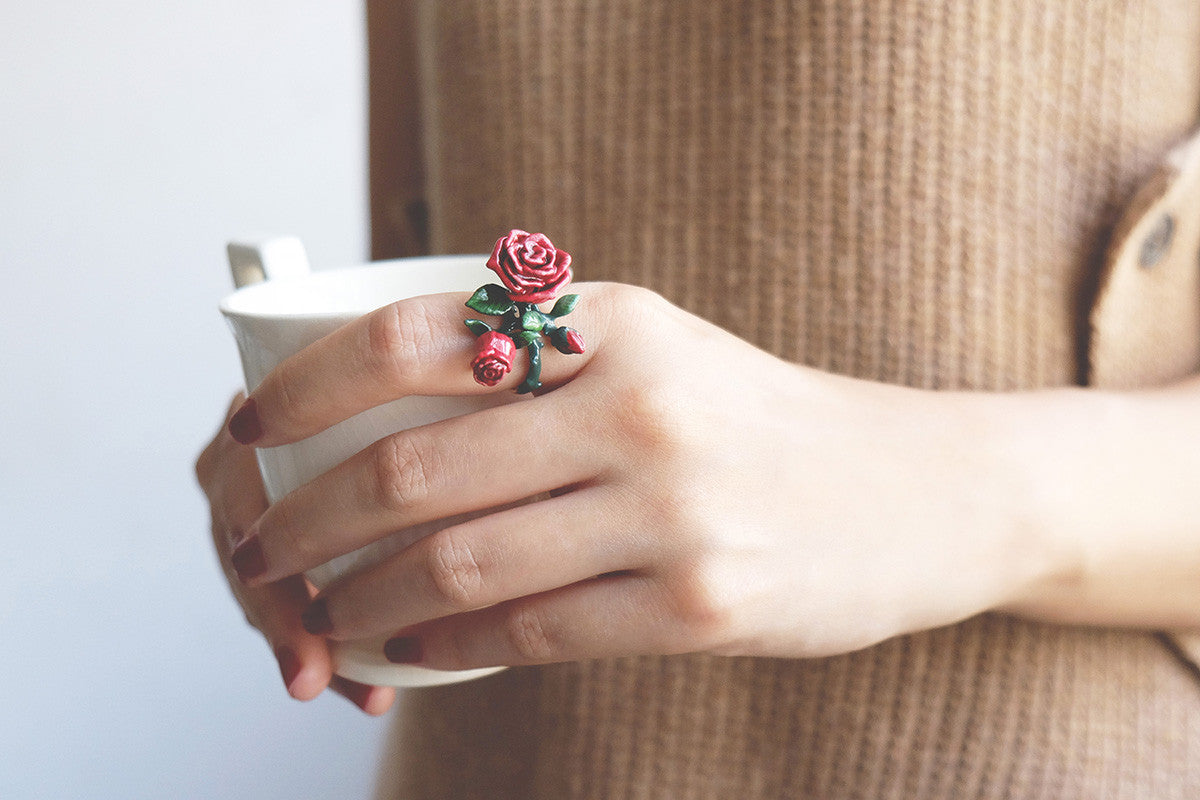 Close-up of a hand with charming rose ring holds a cup of coffee.