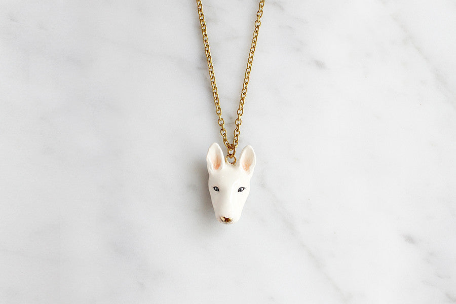 White bull terrier pendant necklace on a gold chain placed on marble background.