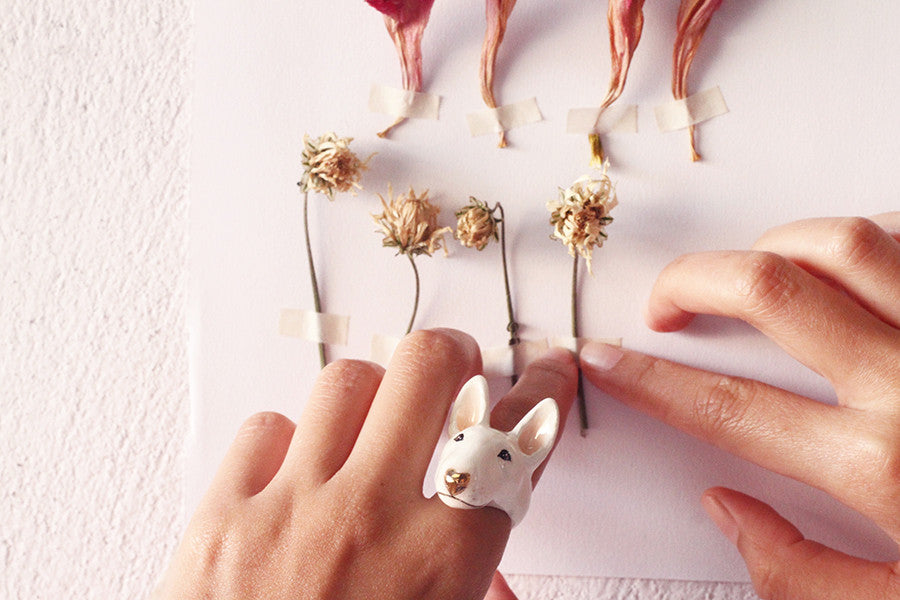 Adorable dog ring on a hand, surrounded by dried flowers on a white background.