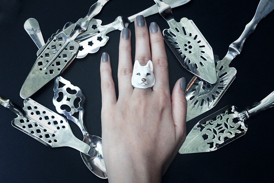 A hand wearing a white husky ring, surrounded by ornate silver serving utensils.