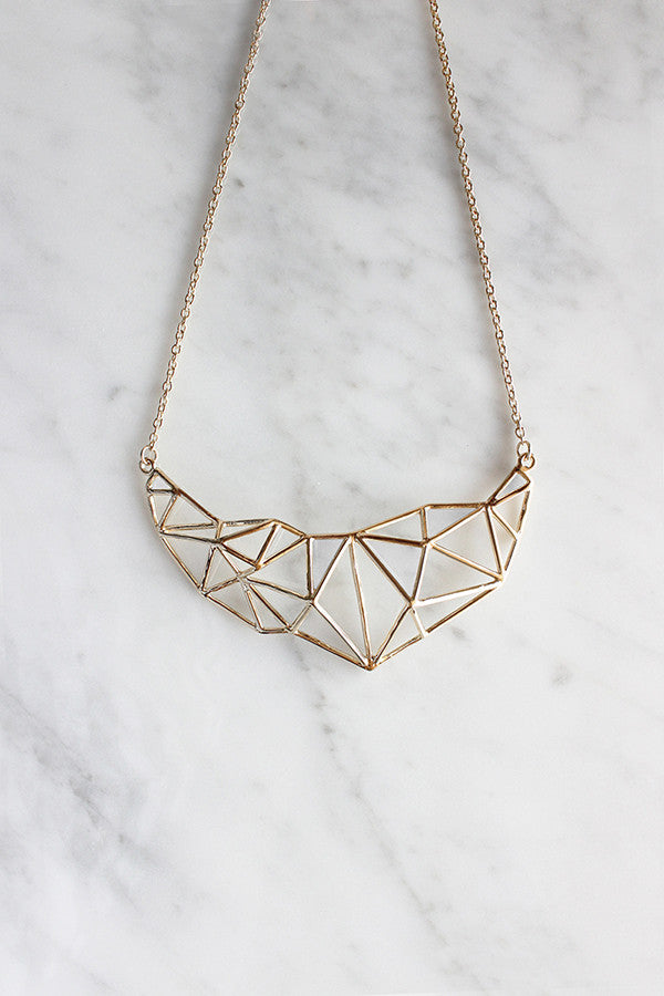 Gold geometric necklace with a triangular pattern placed on a marble background.