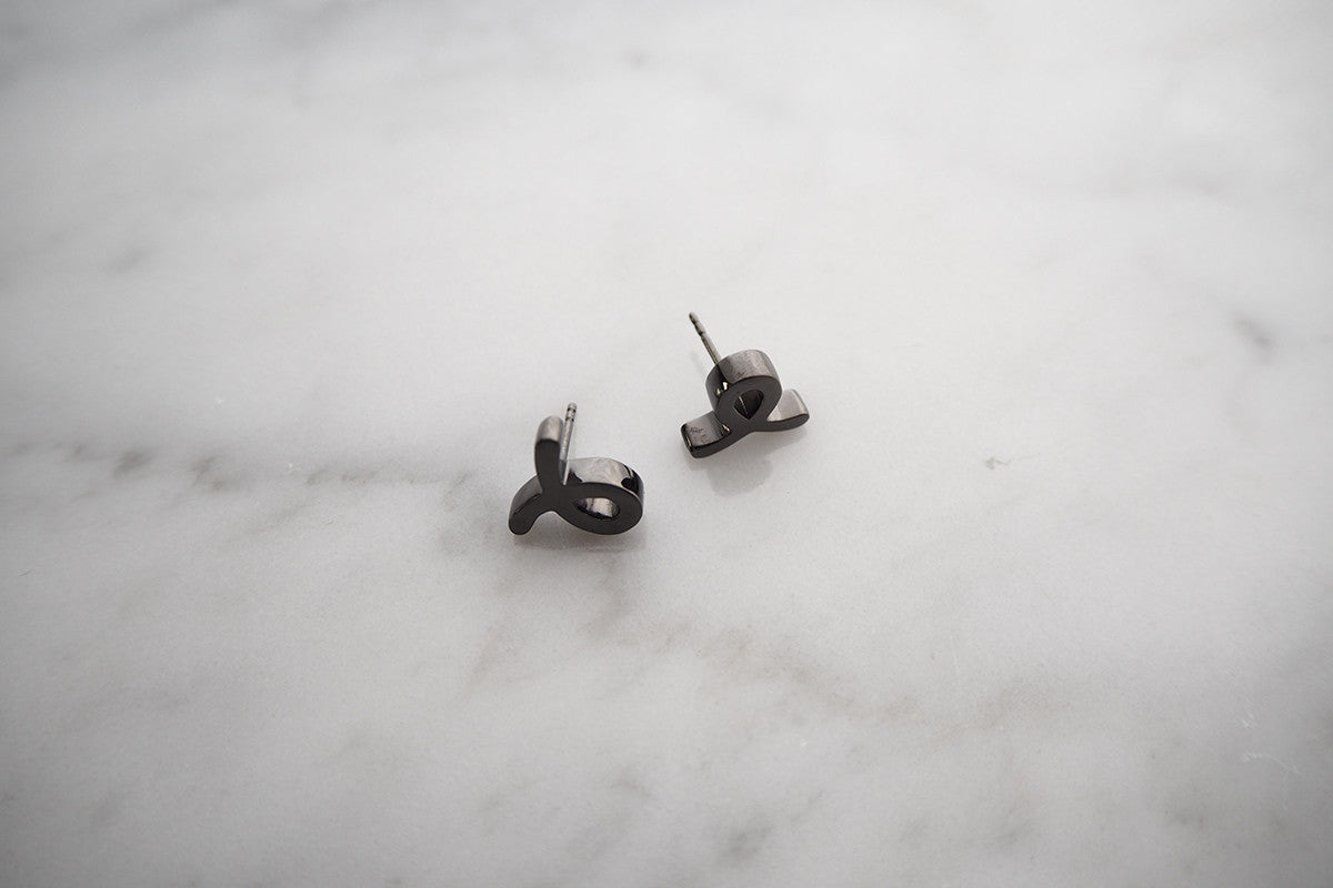 Minimal earrings featuring a unique script-style small "L" design placed on a marble background.