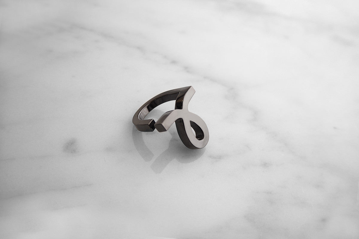 Stylish ring with modern design, showcasing a script-style small "L" design, placed on a marble background.