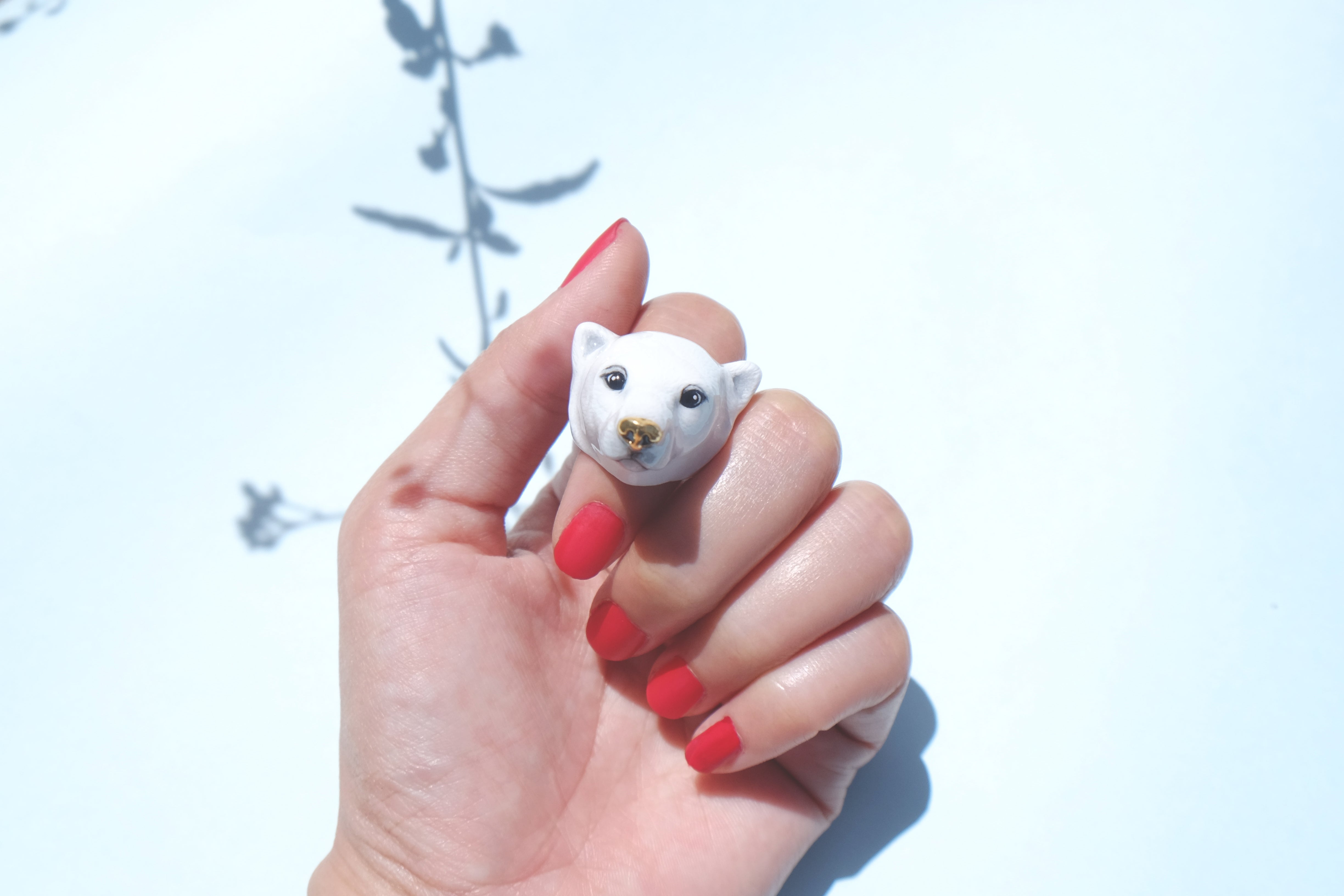 Close up of a hand with red nail polish showcasing an adorable polar bear ring