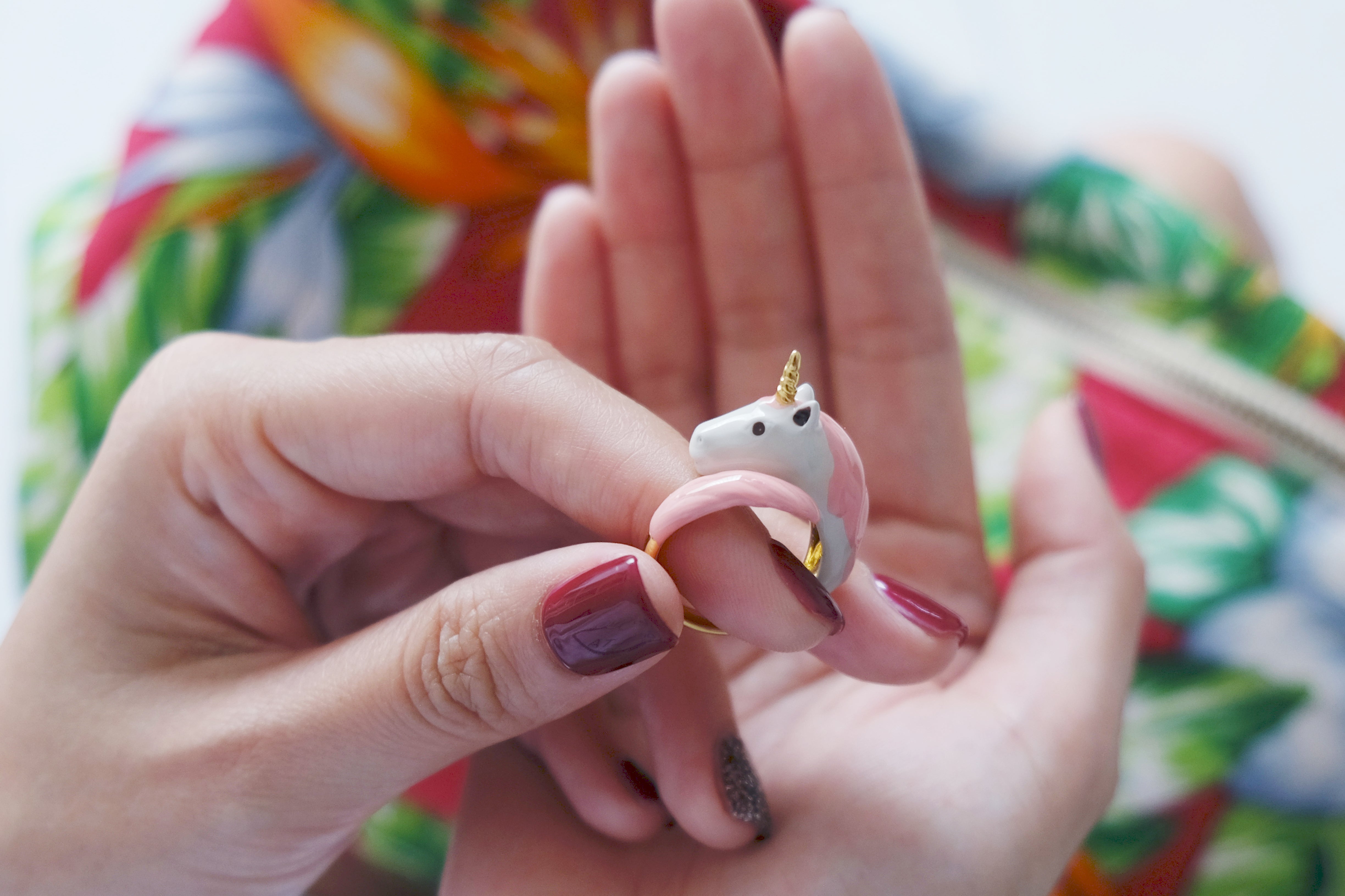 A hand holding a adorable unicorn ring featuring pink and white design