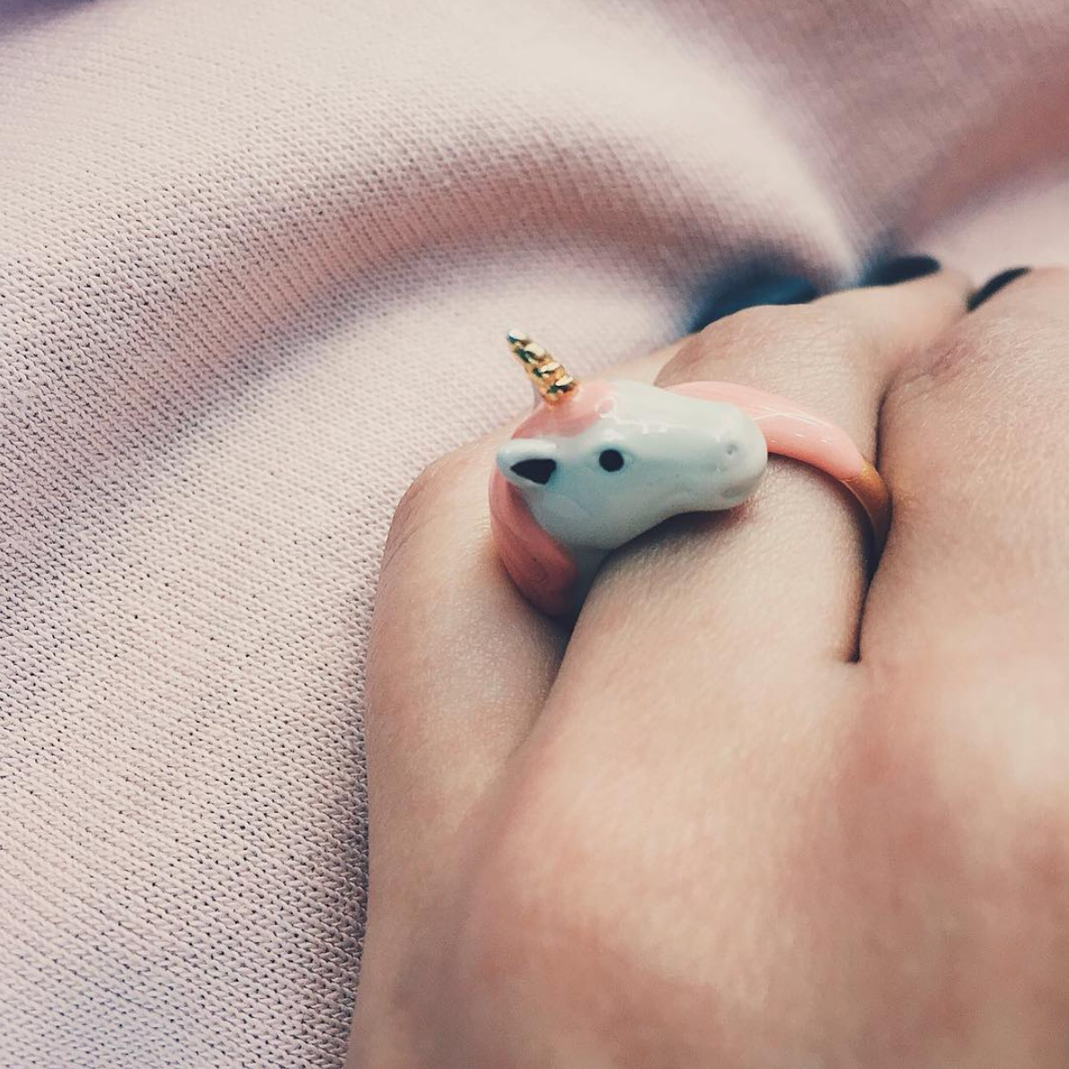 Close up of a hand worn a unique unicorn ring on pastel fabric.