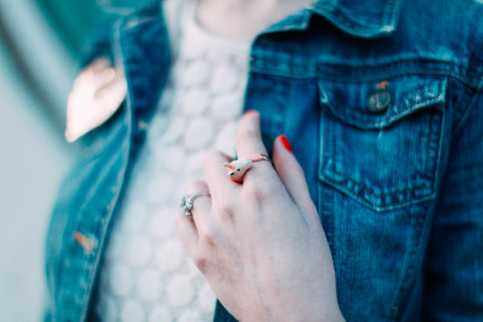 A close-up of a hand with unicorn ring, resting on a denim jacket.

