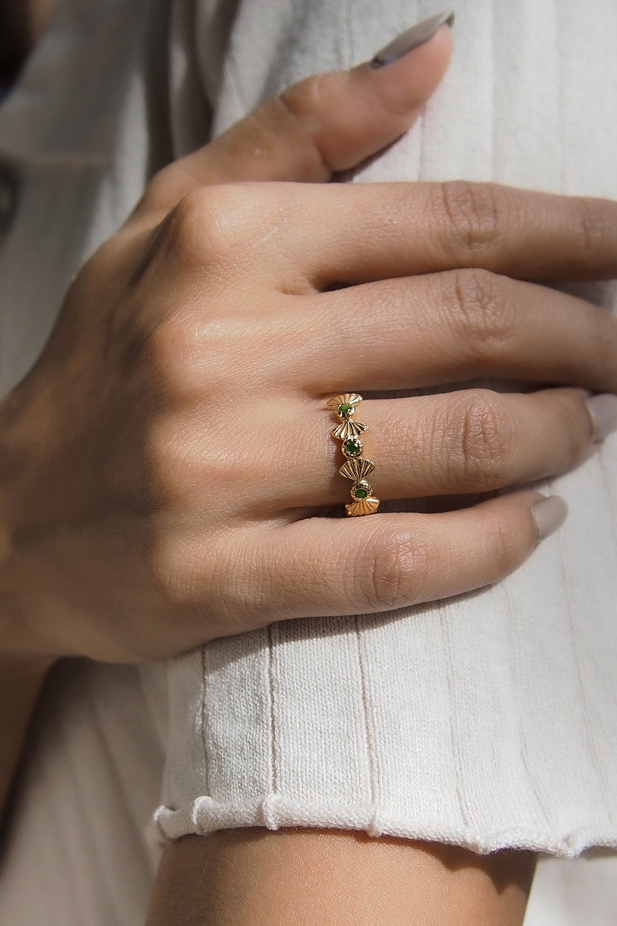 Close-up of a hand wearing a gold ring with green stones
